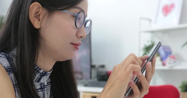 Femme asiatique tapant un message texte sur le téléphone intelligent à la maison. Image recadrée d'une jeune femme assise à une table et utilisant un téléphone portable
. - Séquence, vidéo