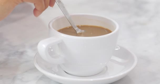 Uma xícara de café, jovem mulher branca asiática por mãos está misturando café com colher metálica em copo de cerâmica branca na mesa de mármore branco
. - Filmagem, Vídeo