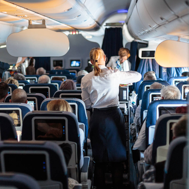 Wnętrze dużego komercyjnego samolotu z stewardesy serwujemy pasażerów na siedzeniach podczas lotu. - Zdjęcie, obraz