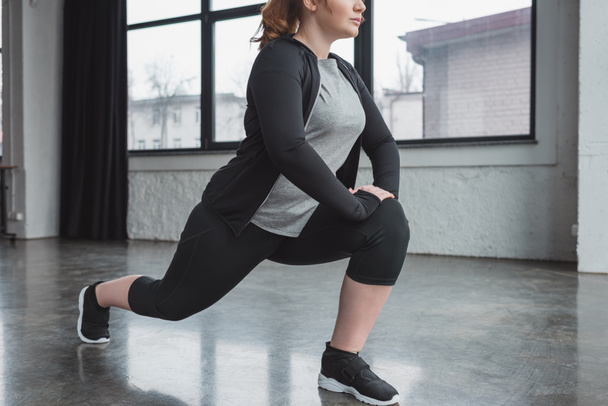 Curvy girl in gym stretching legs - Foto, afbeelding