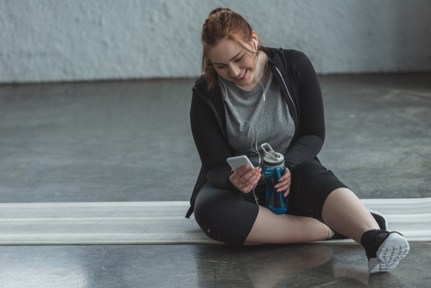 Curvy girl resting and listening to music in gym  - Fotografie, Obrázek