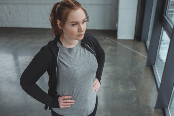 Избыточный вес определяется девушка стоя в тренажерном зале
 - Фото, изображение