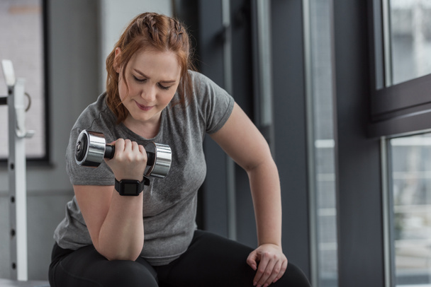 Curvy girl lifting dumbbell in gym - Photo, Image