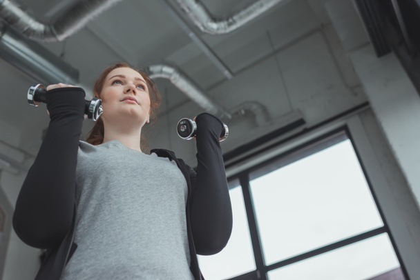 Толстая девушка тренируется с гантелями в спортзале
 - Фото, изображение