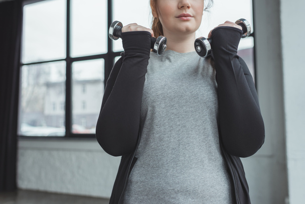 Overweight girl training with dumbbells in gym - Фото, зображення