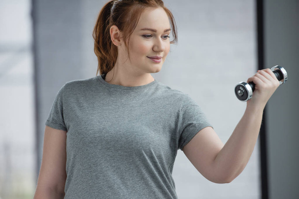 Curvy girl training with dumbbell in gym - Photo, image