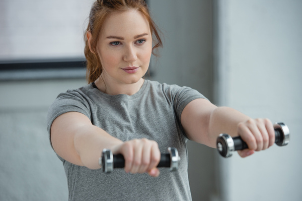 Overweight girl exercising with dumbbells in gym - Photo, Image