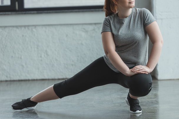 Overweight girl stretching legs in gym - Foto, imagen