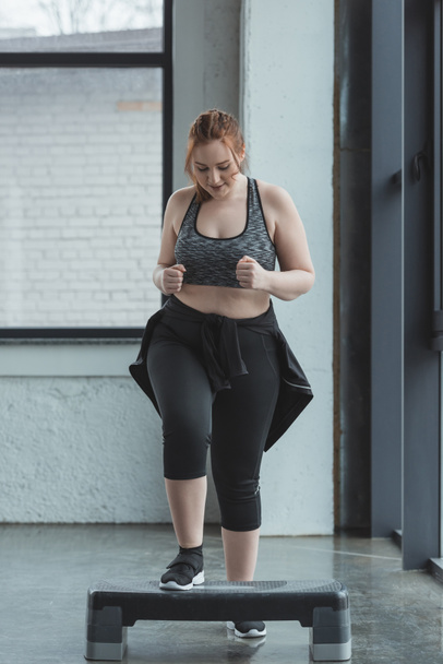Overweight girl jumping on step platform in gym - Valokuva, kuva