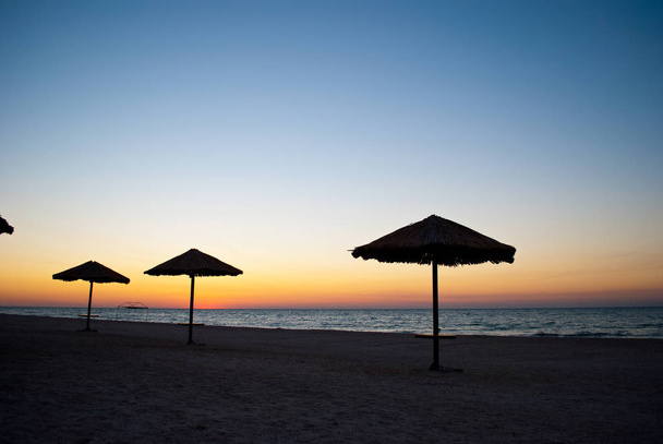 diversi un sacco di ombrelloni grandi di paglia e metallo stand sulla spiaggia sabbia spiaggia blu mare blu cielo estate mattina sera calma
 - Foto, immagini