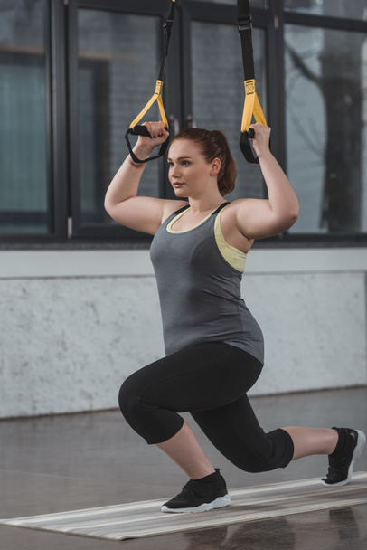 Overweight girl training on resistance band in gym - Photo, Image