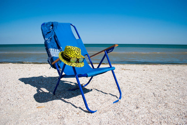 blauer Strandkorb und stylische gelbe Mütze mit Sonnenbrille am Ufer des blauen Meeres blauer Himmel weiße Wolken schöne Landschaft Sommerurlaub Strand Wochenende Erholung Ufer - Foto, Bild