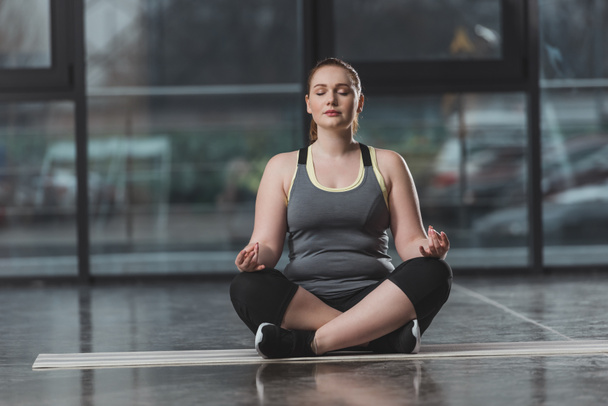 Curvy girl during meditation in gym - Photo, Image