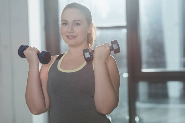 Overweight girl training with dumbbells in gym - Foto, Bild