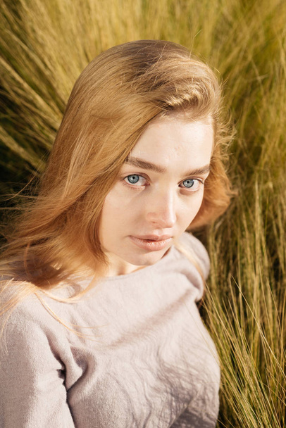 young blue-eyed girl blond model posing, sitting in a field in the sun - Photo, image