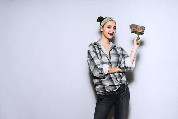 happy beautiful girl in a plaid shirt paints the wall with a brush in her apartment - Fotó, kép