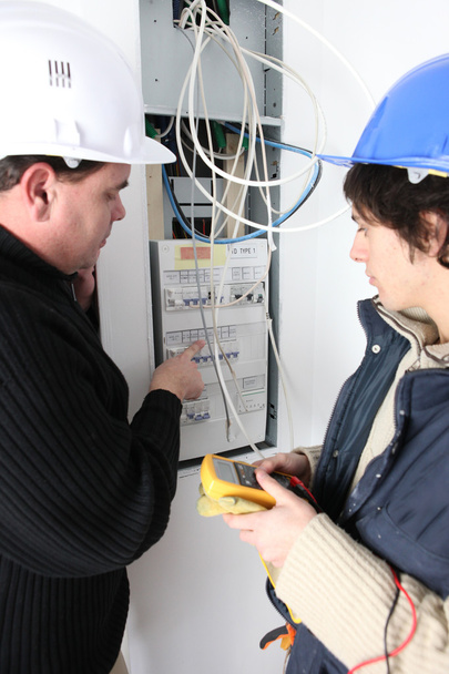 Kaksi sähkömiestä korjaamassa sulakerasiaa
 - Valokuva, kuva