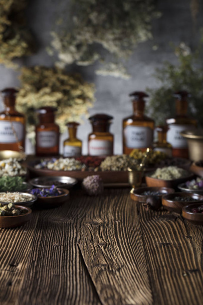 Natural medicine background. Brass mortar, bottles. Rustic table. Assorted dry herbs in bowls. Bokeh. - Photo, Image