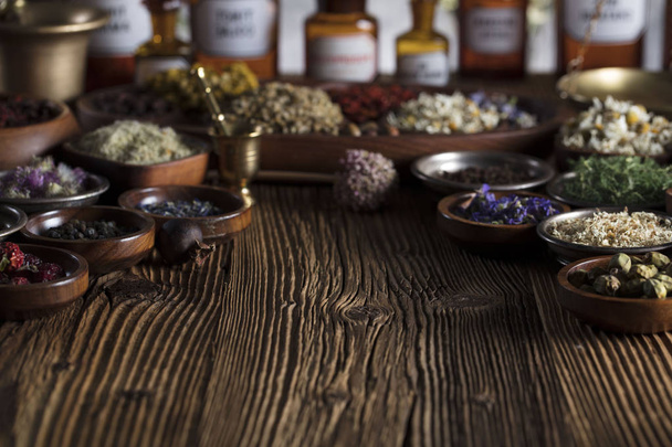 Natural medicine background. Brass mortar, bottles. Rustic table. Assorted dry herbs in bowls. Bokeh. - Photo, Image