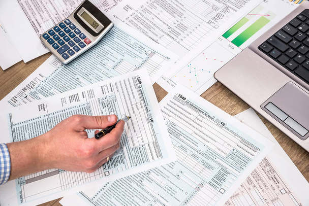 Businessman  filling 1040 tax form with help laptop at office desk - Fotoğraf, Görsel