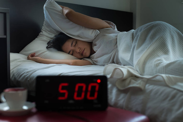 Молодая азиатская женщина получает стресс просыпаясь рано утром в 5 часов, будильник
 - Фото, изображение
