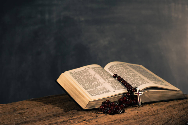 Священное библейское распятие и бусы на старом деревянном столе из дуба. Темный задний план.
 - Фото, изображение