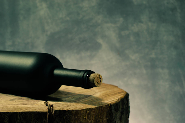 Black bottle of red wine on a round, cracked wooden table. - Fotoğraf, Görsel