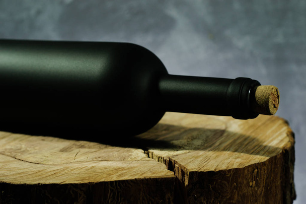 Black bottle of red wine on a round, cracked wooden table. - Photo, Image