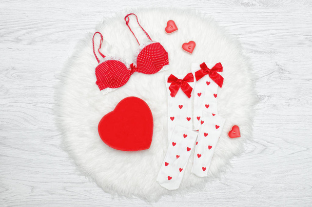 Έννοια της μόδας. Κόκκινο σουτιέν, λευκές κάλτσες και κουτί σε σχήμα καρδιάς. Λευκή γούνα - Φωτογραφία, εικόνα