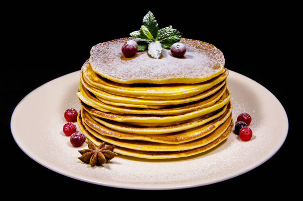 Fresh pancakes on a white plate sprinkled with sugar powder on them lies the cranberry and mint next to the bowl plate - Photo, Image