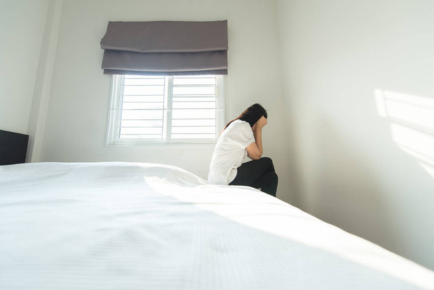 Femme ont un mal de tête et se sentent sérieux tout en étant assis sur le lit après le réveil le matin
 - Photo, image