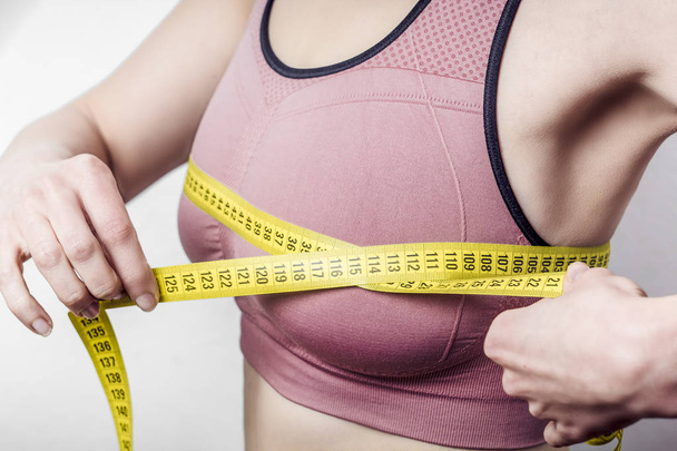 The concept of diet, weight loss. Closeup of young woman measures her breast with a measuring tape. - Foto, afbeelding