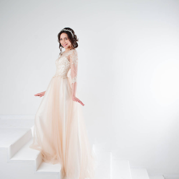 Portrait of a beautiful girl in a wedding dress. Bride in a luxurious dress standing on the stairs, climb up - Fotó, kép
