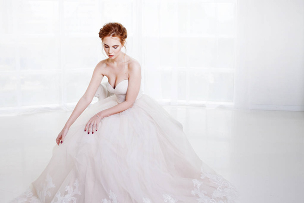 Portrait of a beautiful girl in a wedding dress. Bride in luxurious dress sitting on a chair - Фото, зображення