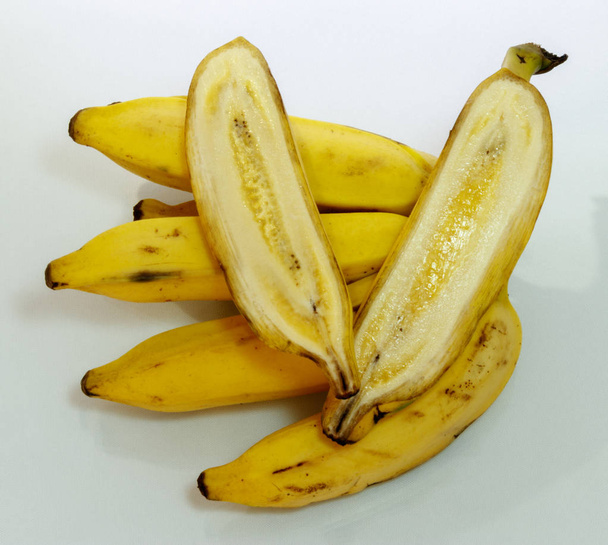 Joukko trooppisia keltaisia banaaneja, syötäviä kypsiä hedelmiä, yksi leikattu keskellä, valkoisella pohjalla
. - Valokuva, kuva