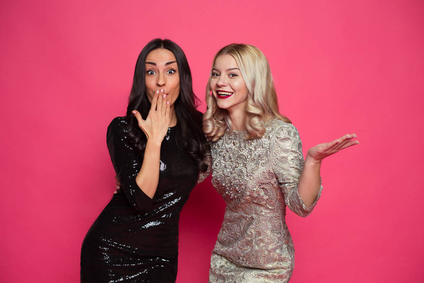 Friends forever. Close up photo of Two happy young beautiful smiling girlfriends in little black dresses posing and having fun on a pink background. - Фото, зображення