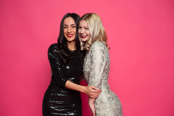 Friends forever. Close up photo of Two happy young beautiful smiling girlfriends in little black dresses posing and having fun on a pink background. - Fotoğraf, Görsel