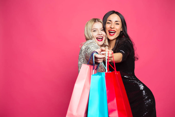 Shopping concept. Girl friends on shopping. Two cheerful beautiful smiling women with shopping bags on a pink background. - Fotografie, Obrázek