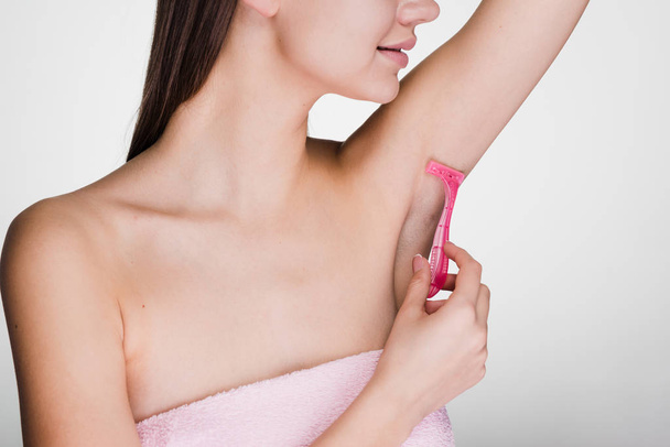 cute young girl shaves her hair on her armpits with a pink razor - Fotografie, Obrázek