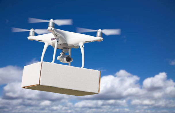 Drone Quadcopter du système d'aéronef sans pilote (UAS) transportant un paquet blanc dans les airs
. - Photo, image