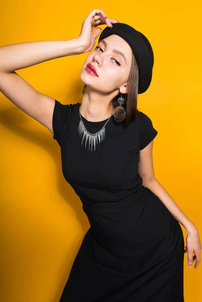 beautiful attractive model girl in fashionable black hat posing on yellow background, expensive jewelry - Foto, Imagem