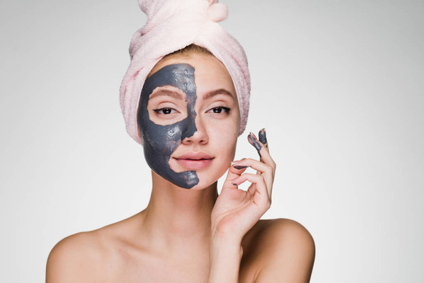a young attractive girl with a pink towel on her head applied a useful clay mask to half the face - Foto, Bild