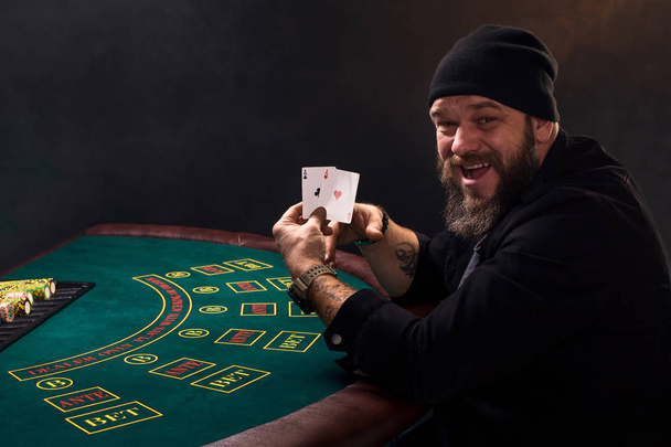 Γενειοφόρος άνδρας που δείχνει τα χαρτιά του πόκερ σε μαύρο φόντο - Φωτογραφία, εικόνα