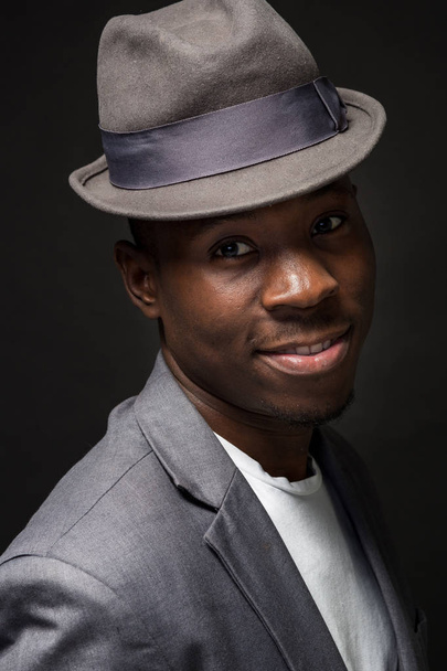 Muotokuva houkutteleva nuori musta mies studio hattu cheesy hymy tumma tausta
 - Valokuva, kuva