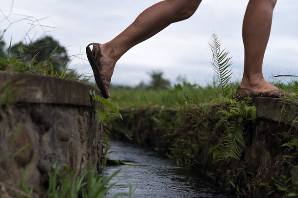 Caucasian woman step over the water ditch. Se has an active vacation in asia and goes for a walk - Photo, Image