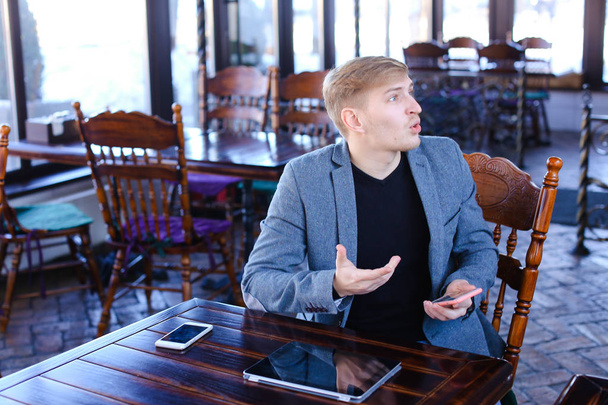 Бизнесмен сидит рядом со столом со смартфоном и ноутбуком Speaki
 - Фото, изображение