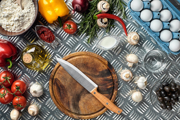 Cutting wooden board with traditional pizza preparation ingredients: mushrooms, tomatoes sauce, basil, olive oil, cheese, spices. Iron texture table background - Foto, Imagem