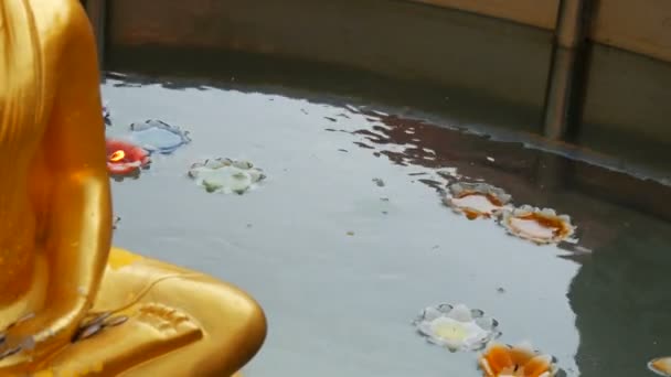 Aranyozott Buddha-szobor, amely úszó körül sokszínű viasz gyertya, az alakja egy lotus - Felvétel, videó