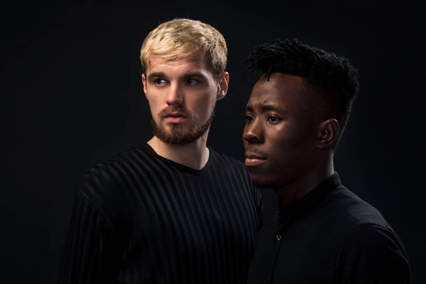 Portrait of two young african american and caucasian men standing over black background. Studio shot - Fotoğraf, Görsel