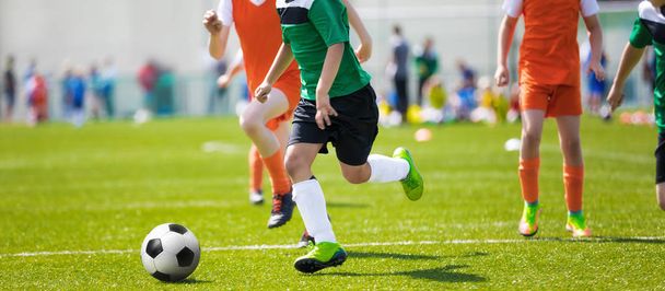 Fußballspieler laufen. Fußballer kicken Fußballspiel; junge Fußballer laufen dem Ball hinterher. Fußballer in grünen und orangefarbenen Trikots kicken Fußball  - Foto, Bild